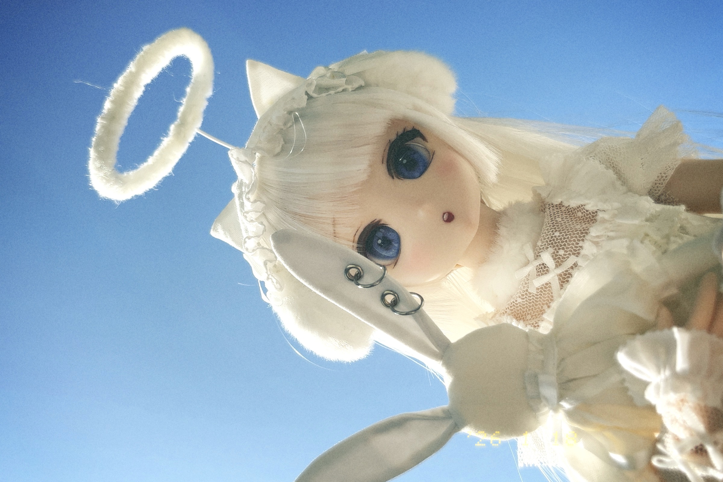 天使の恰好のドールが青空をバックに覗き込む